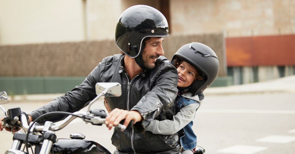 Man riding a motorcycle with a child sitting on the bike behind him.